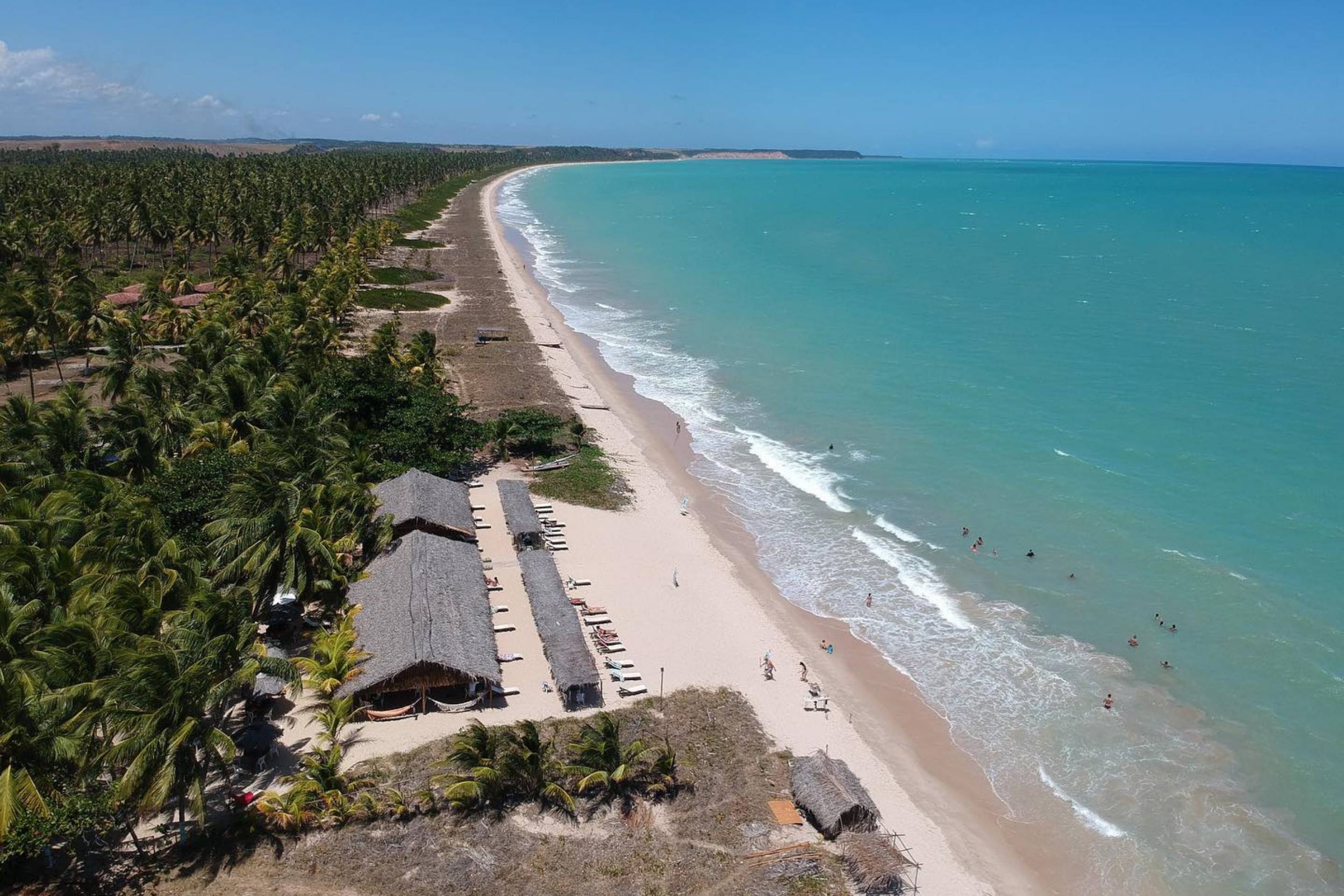 Praia da Barra de Santo Antônio se estende por quilômetros em frente ao mar; as redes e espreguiçadeiras do Restaurante Capitão Nikolas são visíveis