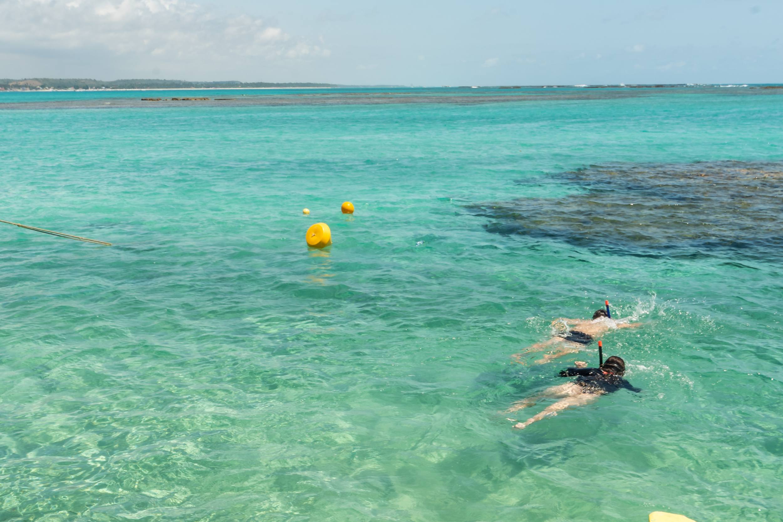 Duas pessoas flutuam na água, observando o fundo do mar com a ajuda de snorkels.