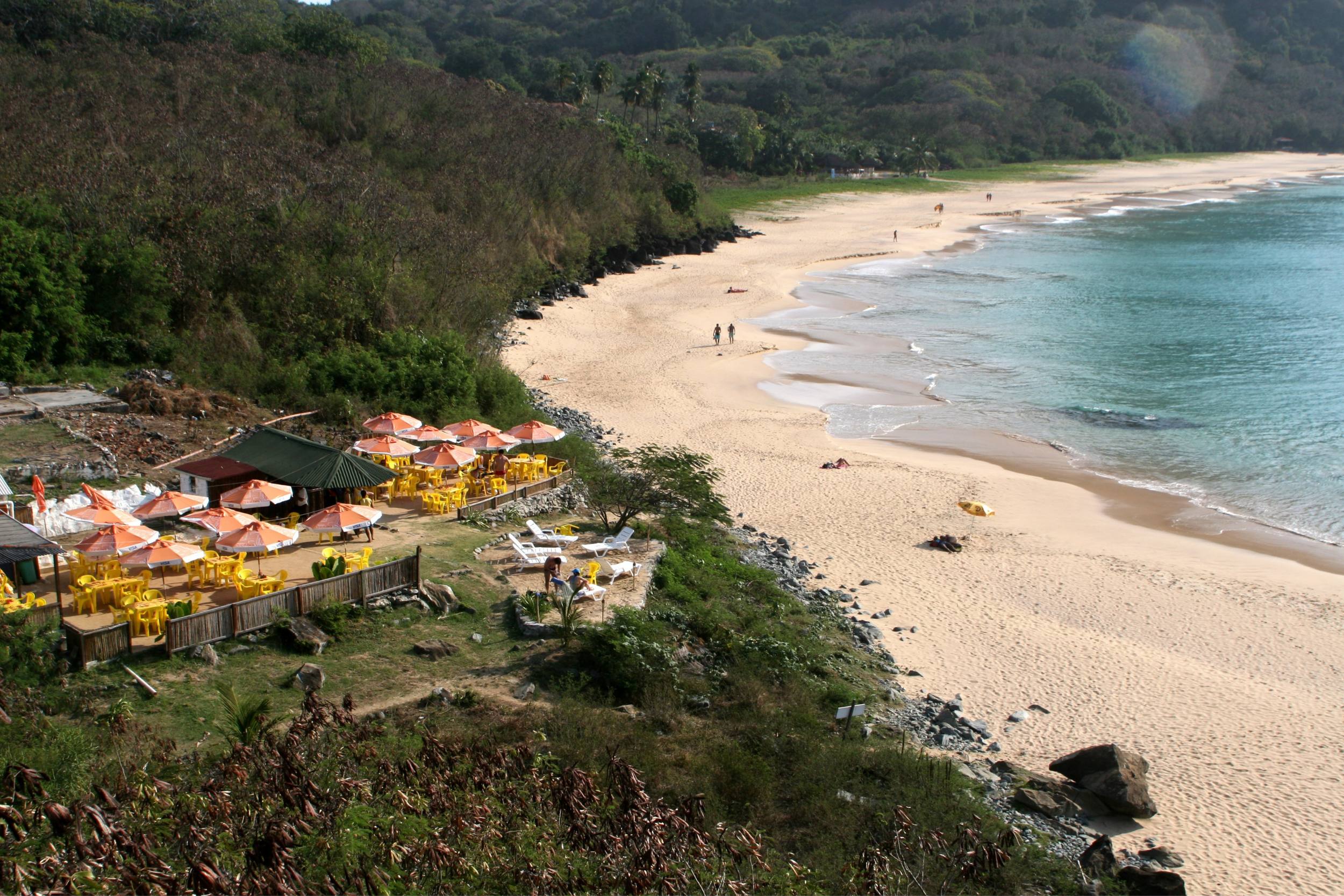 A praia da conceição está retratada, com o Bar do Meio visível do alto de um morro sobre a praia.