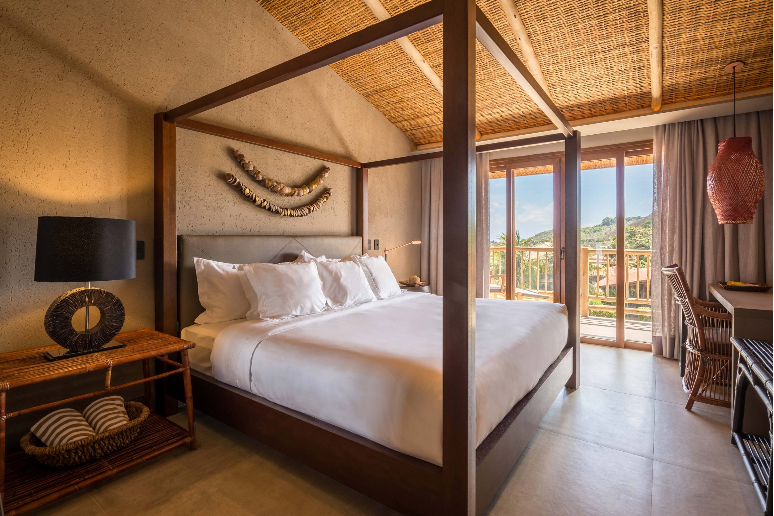 Cama com dossel iluminada por luz natural através das portas de vidro da varanda.